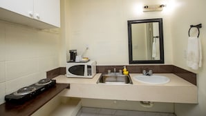 A compact kitchen with a stove, microwave, sink, and a mirror above the sink. - Camrose Motel (Camrose)