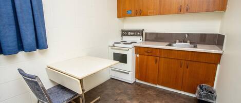 Una pequeña kitchenette equipada con estufa, horno y lavaplatos. Incluye una mesa plegable y una silla.