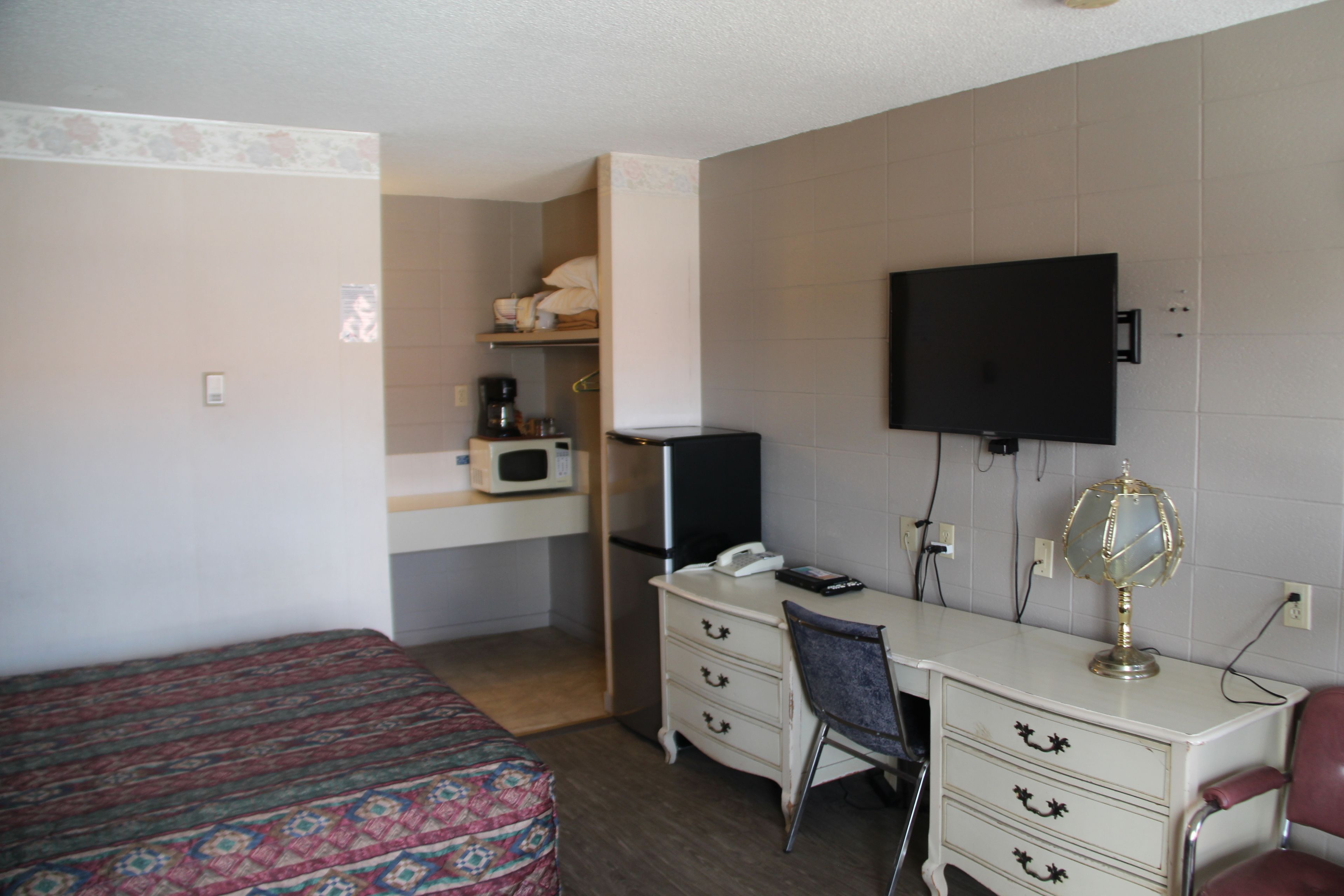 Una habitación de hotel con cama, escritorio con silla, televisor, cómoda y microondas.