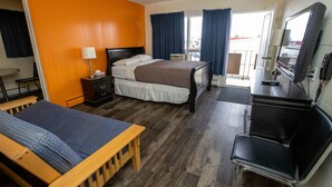 A hotel room with two beds, a desk, a chair, a TV, and a balcony with curtains. - Camrose Motel (Camrose)