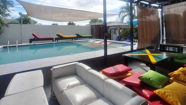 An outdoor pool area with lounge chairs and a covered seating area. - Labrish Guest House (Kingston)