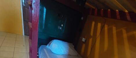 Una habitación pequeña y funcional con una cama individual, cabecera de madera y suelo de baldosas.