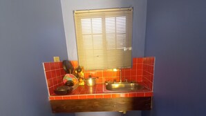 A kitchen with a blue wall, a window with blinds, a sink, and a countertop with a pot and a ladle. - Labrish Guest House (Kingston)