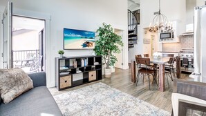 A spacious living area with a large window, a dining table, and a kitchen.