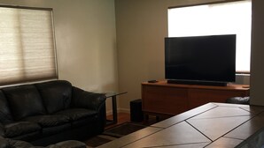 Uma sala de estar com um sofá de couro preto, uma TV de tela plana em um suporte de madeira e um balcão de pedra.
