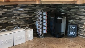Uma cozinha com armários de madeira, cafeteira e recipientes identificados para farinha, açúcar e chá.