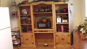 Un armadietto da cucina in legno con ripiani, un forno a microonde e diversi oggetti per la cucina.