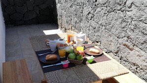 Ein draußen aufgebautes Frühstücksbuffet mit Holztisch, verschiedenen Speisen und einer Steinmauer im Hintergrund.