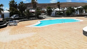 Ein Schwimmbad mit gefliestem Deck, Palmen und blauem Himmel.