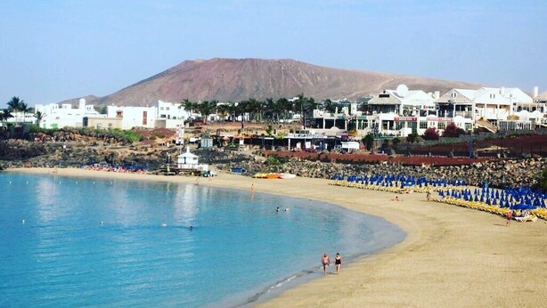 Ein Küstenort mit Strand, weißen Gebäuden und einem Berg im Hintergrund.