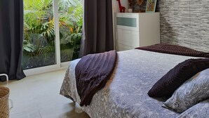 Ein Schlafzimmer mit einem Bett, einer Kommode, einem an der Wand montierten Fernseher und Blick auf Grünflächen.
