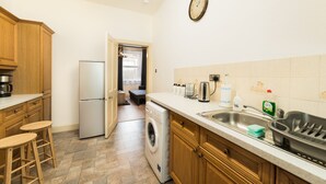 Une cuisine compacte dotée de meubles en bois, d’un réfrigérateur en acier inoxydable, d’un lave-linge et d’un évier avec un égouttoir à vaisselle.