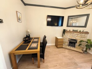 A dining area with a wooden table and chairs, a flat-screen TV mounted on the wall, a fireplace with a stone facade, and a mirror above it.