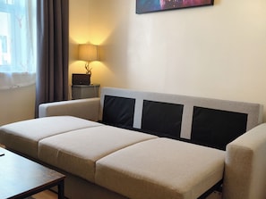 Een moderne woonkamer met een bank, een bijzettafeltje, een lamp en een schilderij aan de muur.