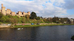 Un château historique, avec une rivière au premier plan, entouré de verdure et de bâtiments résidentiels.
