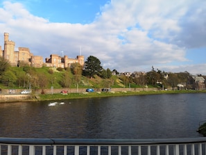 A historic castle with a river in the foreground, surrounded by greenery and residential buildings. - STAG city centre studio apartment (Inverness)