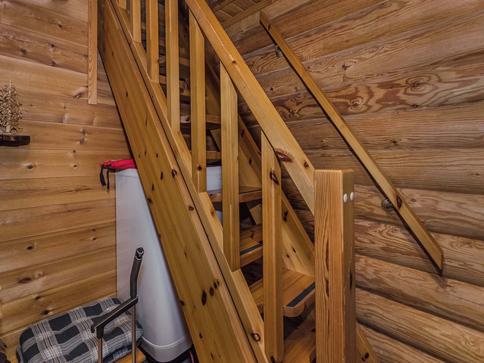 A wooden staircase in a cabin with a white storage box and a red bag on the floor.
