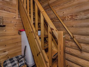 A wooden staircase in a cabin with a white storage box and a red bag on the floor.