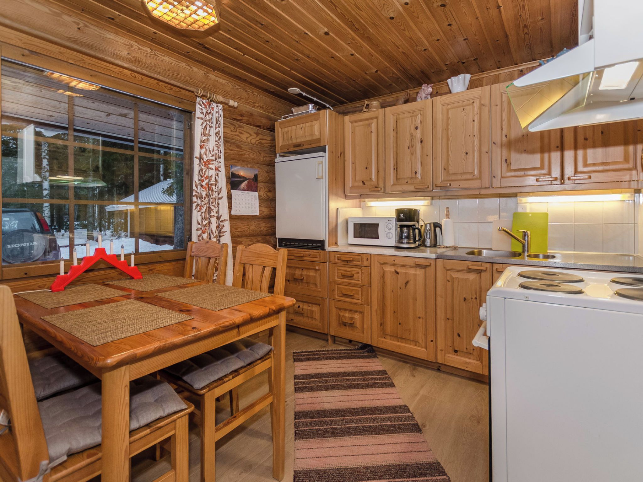 Ein Holzblockhaus-Interieur mit Esstisch, Stühlen, einem Kühlschrank, einer Mikrowelle, einer Kaffeemaschine und einem Herd.