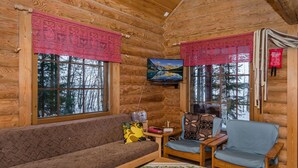 A cozy cabin interior with a wooden interior, a sofa, two chairs, a small table, and a television on the wall.