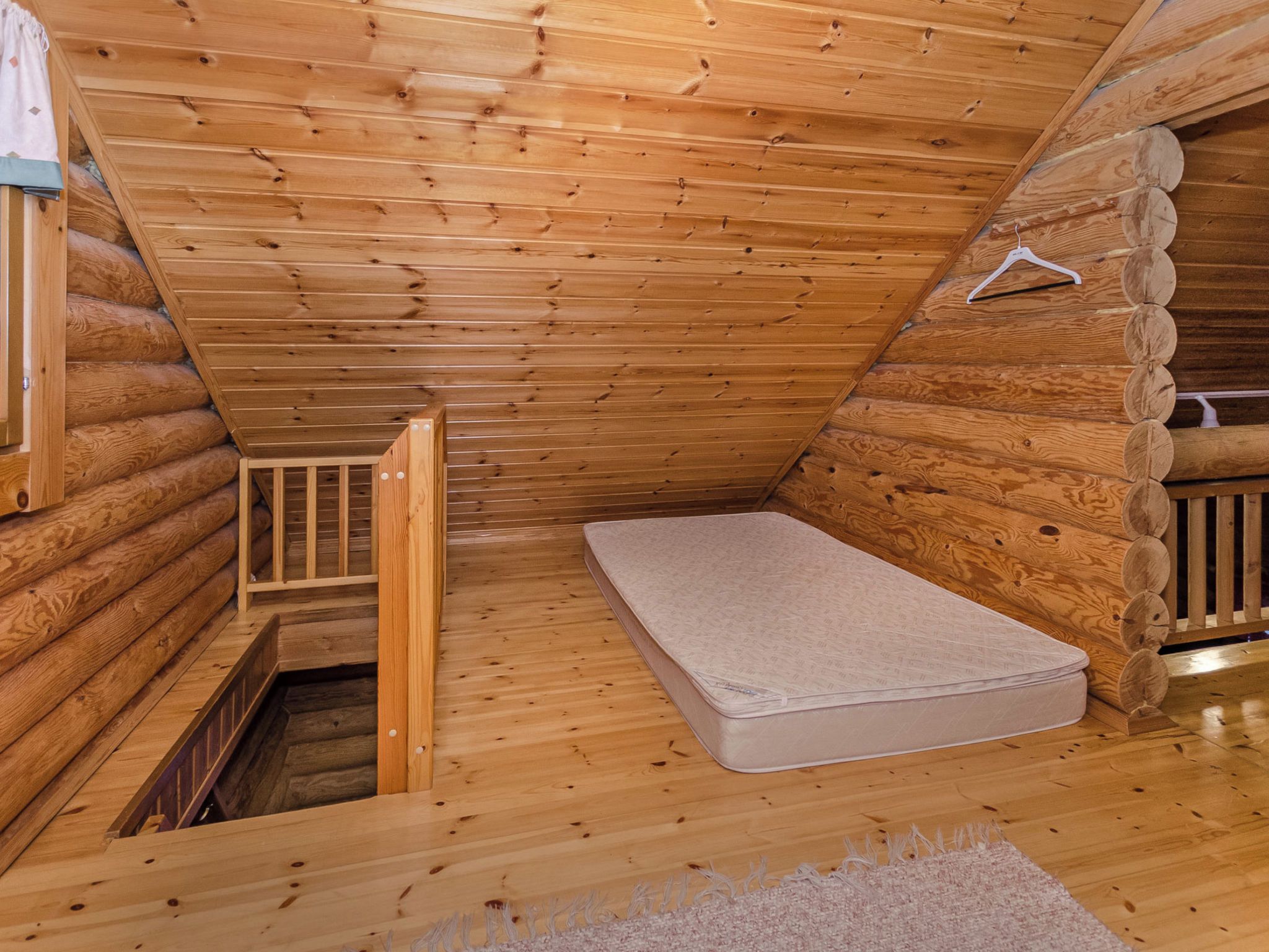 Une chambre aménagée dans une cabane en rondins, avec un matelas simple, une échelle en bois et une petite fenêtre.