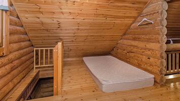 A log cabin room with a single mattress, a wooden ladder, and a small window.