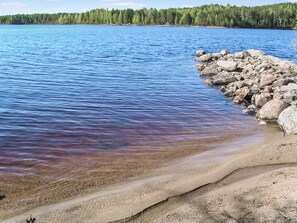 A lake with clear water, a sandy beach, and a rocky shoreline.