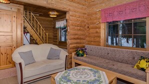 A cozy log cabin interior with a sofa, a small table, and a staircase leading to a loft.