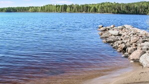 A clear lake with a rocky shoreline and a forest in the background.