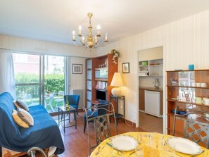 A cozy living room with a sofa, a dining table set, a small kitchen, and a balcony with a view.