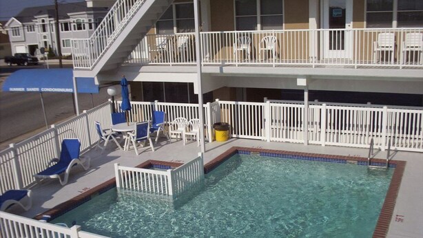 A pool area with clear water, white railings, and lounge chairs. - Beach Block Wildwood Crest Condo (Wildwood Crest)