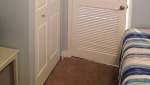 A room with a closed white door, a small table, and a bed with striped bedding. - Beach Block Wildwood Crest Condo (Wildwood Crest)