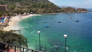 A beach with boats, a sandy shore, and a forested hill.