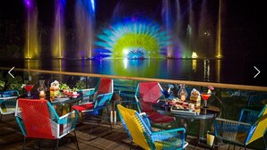 A nighttime outdoor seating area with colorful chairs and a view of a fountain show.