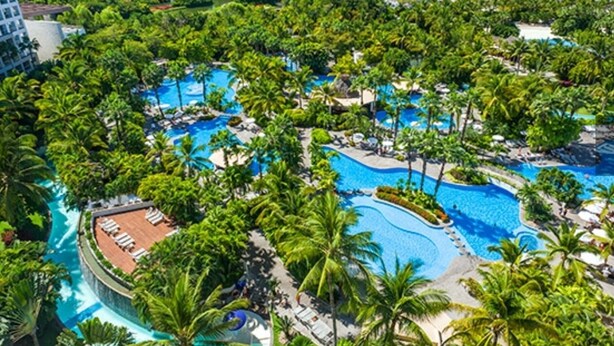 A resort with multiple swimming pools surrounded by lush greenery and palm trees.