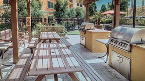 Eine Terrasse im Freien mit Grill, Sitzgelegenheiten und Blick auf den umliegenden Garten und die Gebäude.