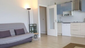 Ein modernes Wohnzimmer mit einem grauen Sofa, einer Stehlampe und einer Küchenzeile mit Schränken und einem Geschirrspüler.