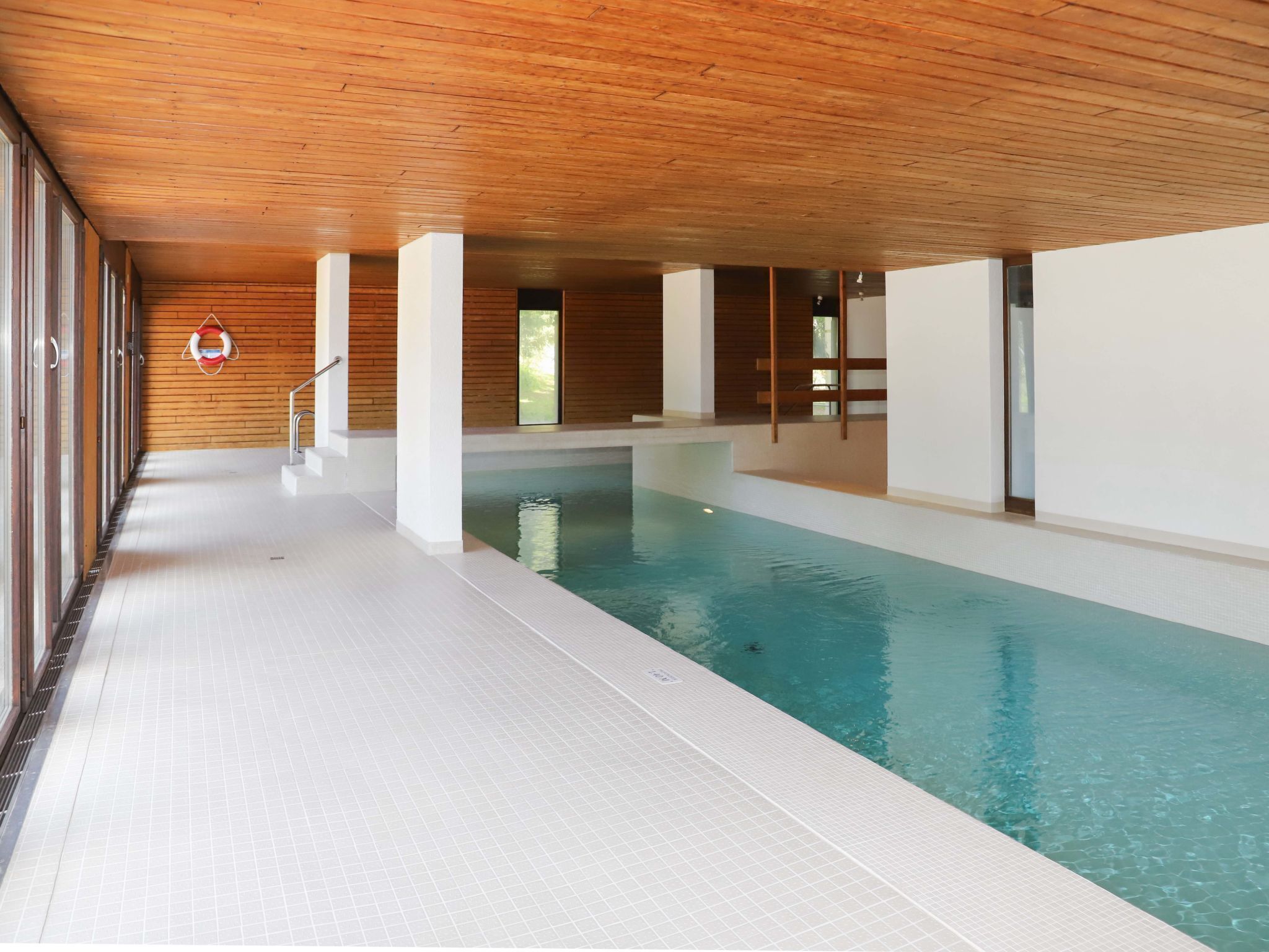 An indoor swimming pool with a wooden ceiling and tiled floor.