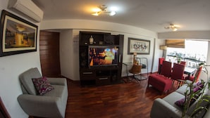 A living room with a flat-screen TV, a grey sofa, a red chair, and a wooden floor. - Inkaclub Miraflores (Lima)