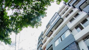 A modern multi-story building with a black metal fence, a sidewalk, and a tree. - Inkaclub Miraflores (Lima)