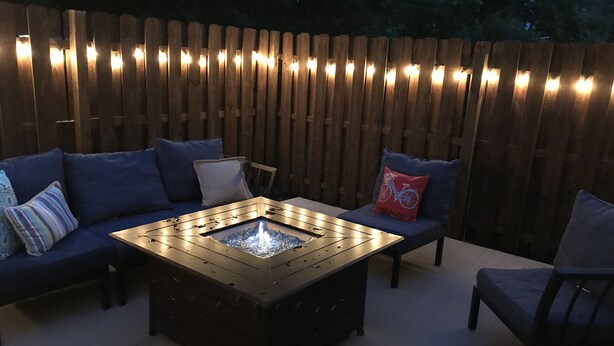 Un espacio exterior con área de estar al aire libre, una mesa con fogón, asientos acolchados y una valla de madera.