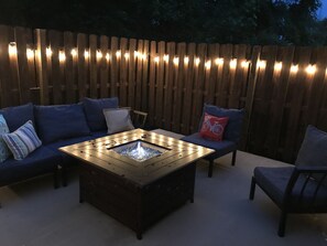 An outdoor seating area with a fire pit table, cushioned seating, and a wooden fence.