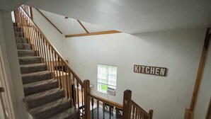 Una escalera con barandales de madera que conduce a un rellano. Un letrero en la pared dice 'KITCHEN'.