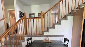Un comedor con mesa y sillas de madera, una escalera con barandillas de madera y un piso de baldosas.