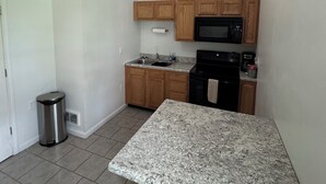 Una cocina compacta con encimeras de granito, armarios de madera, un microondas y una estufa.