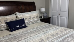 Una cama bien hecha con ropa de cama estampada, un almohilar azul oscuro y una mesita de noche con una lámpara y un cartel que dice 'NO WAKE ZONE'.
