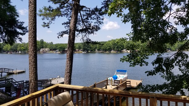 A wooden deck with a chair, overlooking a calm lake with a dock and a boat. - Lake front cottage with dock (Lexington)