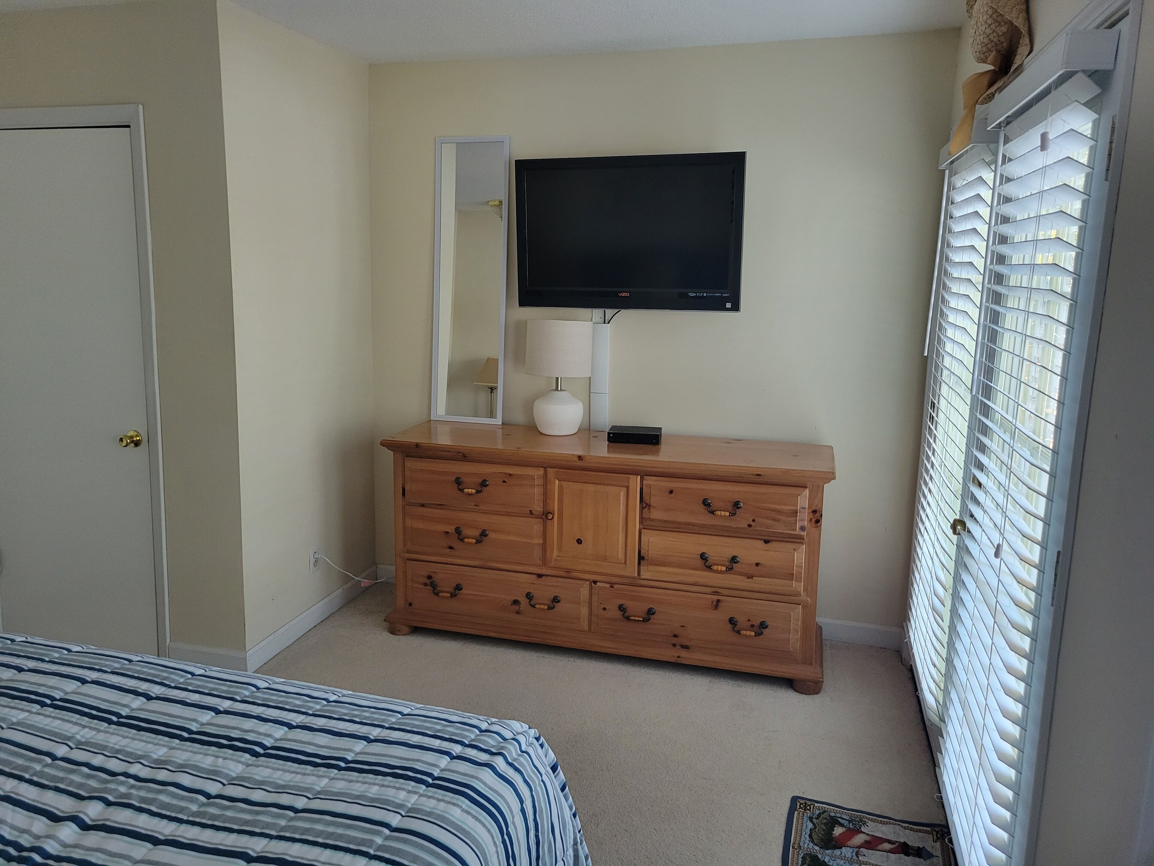Une chambre à coucher avec un lit, une commode en bois, un téléviseur et une fenêtre avec des stores.