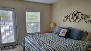 A bedroom with a large bed, two windows with blinds, a wall-mounted lamp, and a decorative wall piece. - Lake front cottage with dock (Lexington)