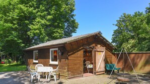 A wooden cabin with a brick patio, a small table with chairs, and a swing set.